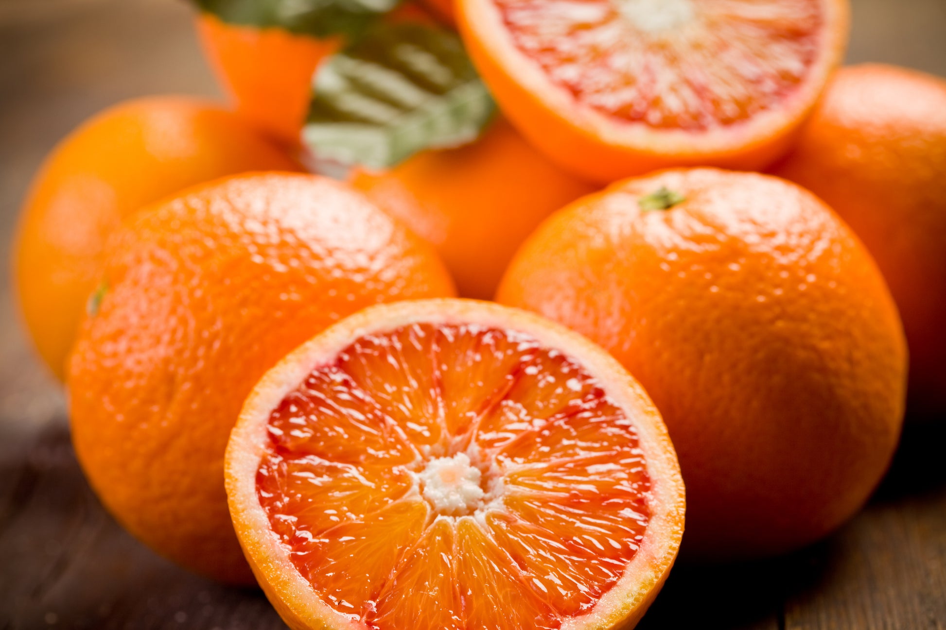 Oranges with one cut open on a wooden surface