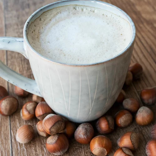 A mug of hazelnut coffee with whole hazelnuts scattered around on a wooden surface.