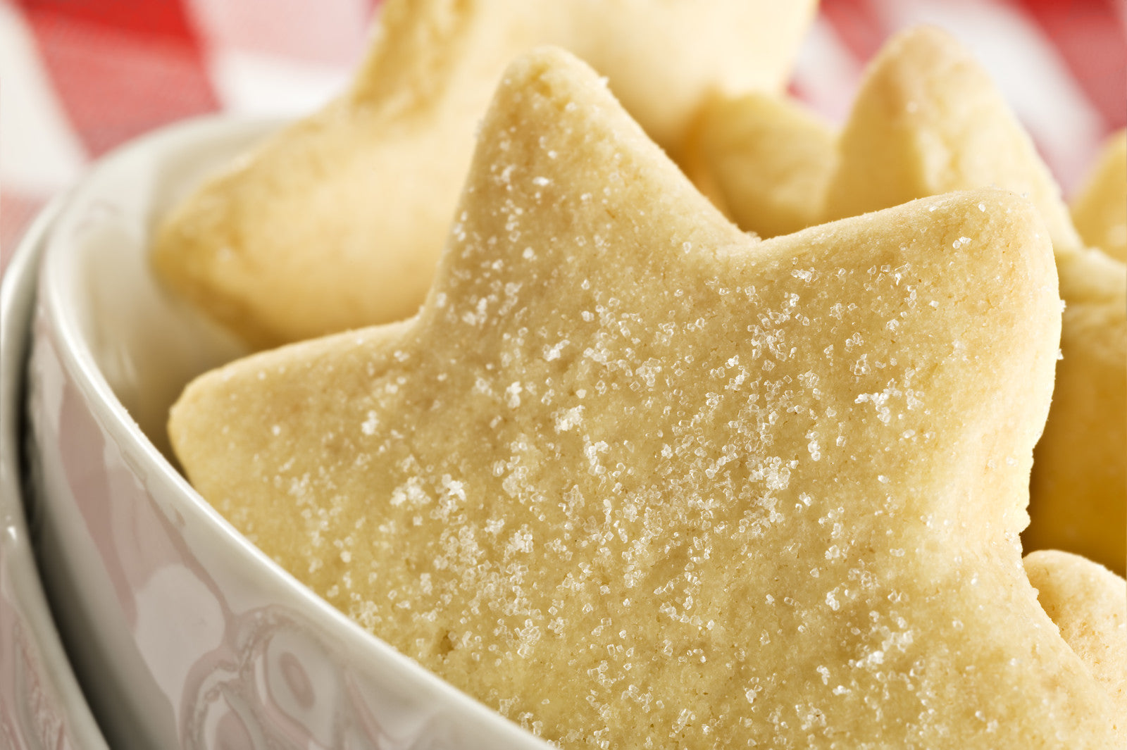 A close-up image of sugar cookies with a dusting of sugar on top, placed in a white bowl.